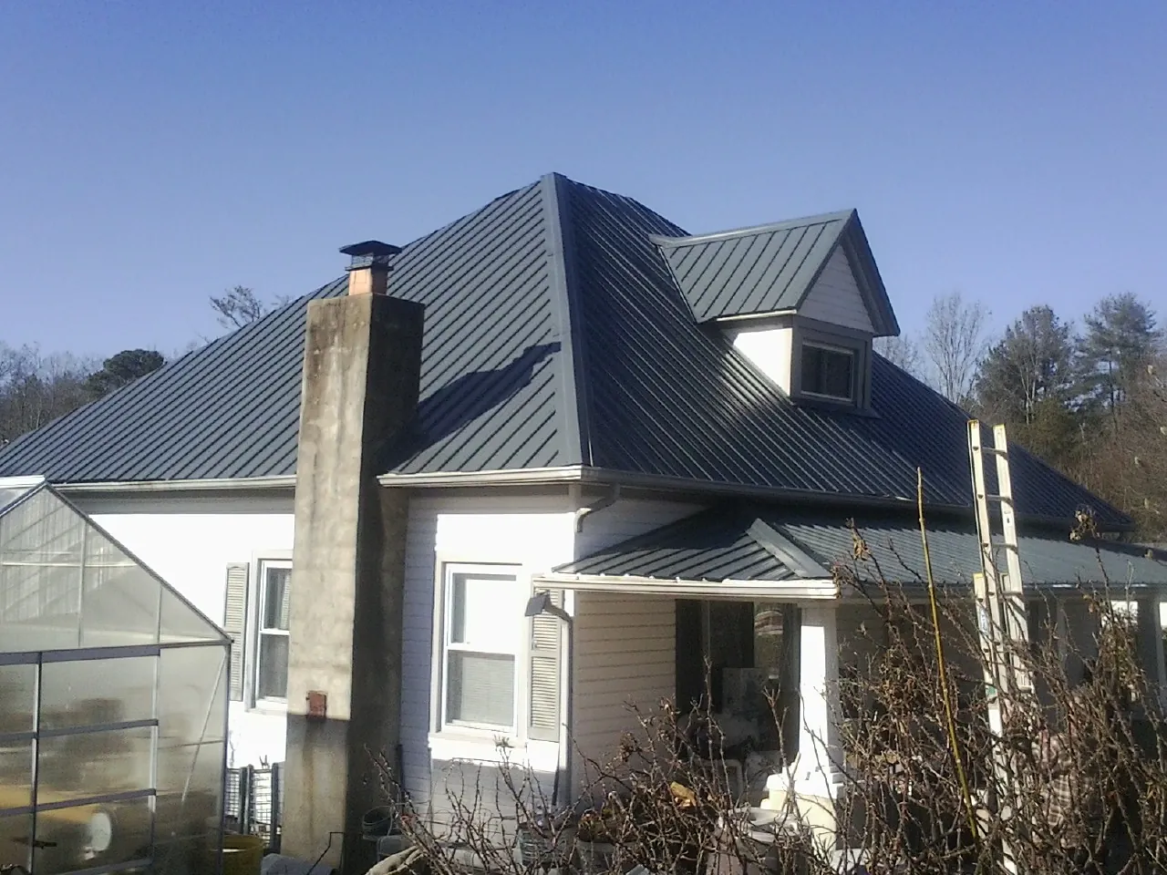 Dark blue standing seam metal roof on a white farmhouse with dormer — Slate & Tile Roof Repair by Roofing Brothers in Melvin
