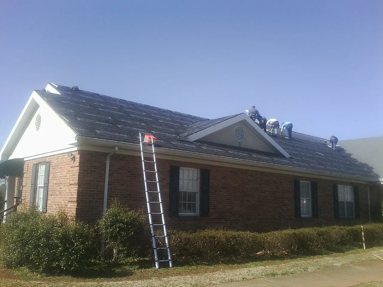 Crew tearing shingles off a brick ranch roof with a ladder set — Emergency Roof Repair work by our crew in Melvin