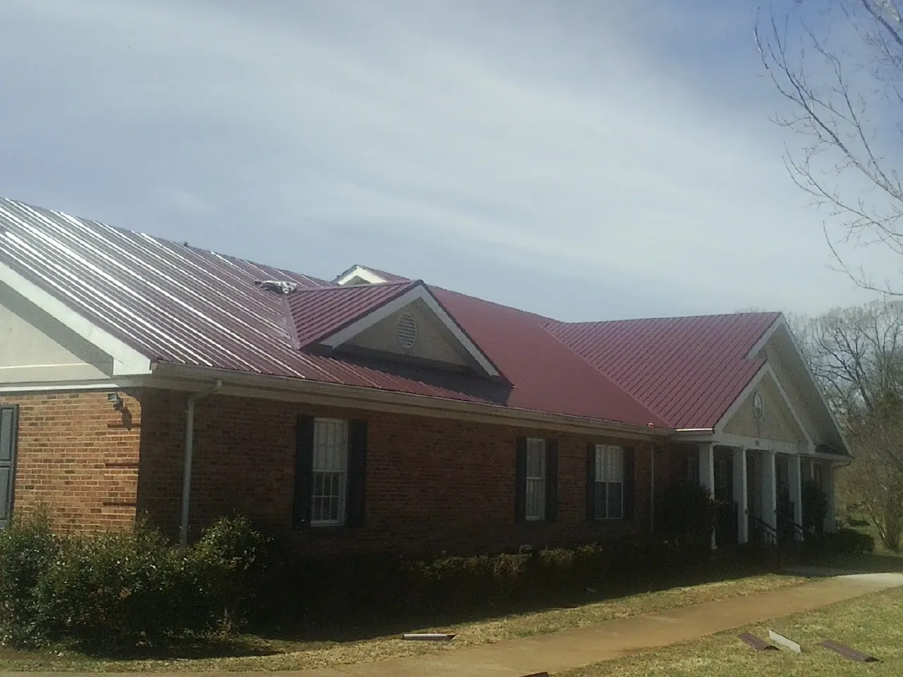 Red metal roof with gabled entries on a long brick building, from a Hail Damage Roof Repair job in Melvin