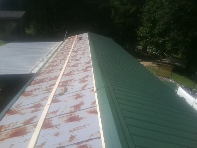 Old rusted panels beside newly installed green metal roofing — Wind Damage Roof Repair by Roofing Brothers in Melvin