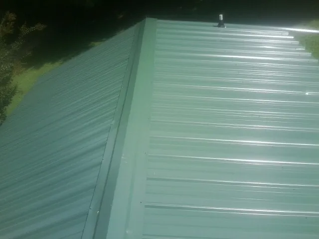 New green metal panels meeting at the ridge of a roof — Flat Roof Repair work by our crew in Melvin