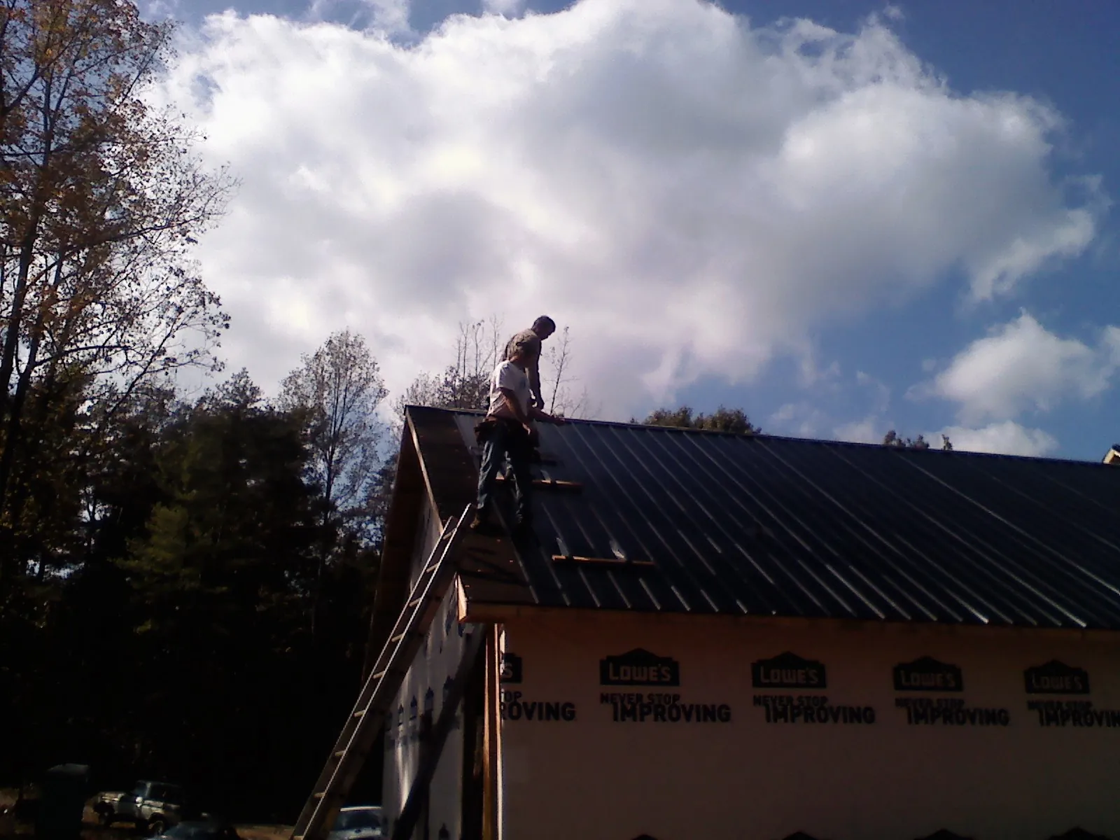 Roofer fastening dark metal panels high against a cloudy sky, from a Roof Inspection job in Melvin