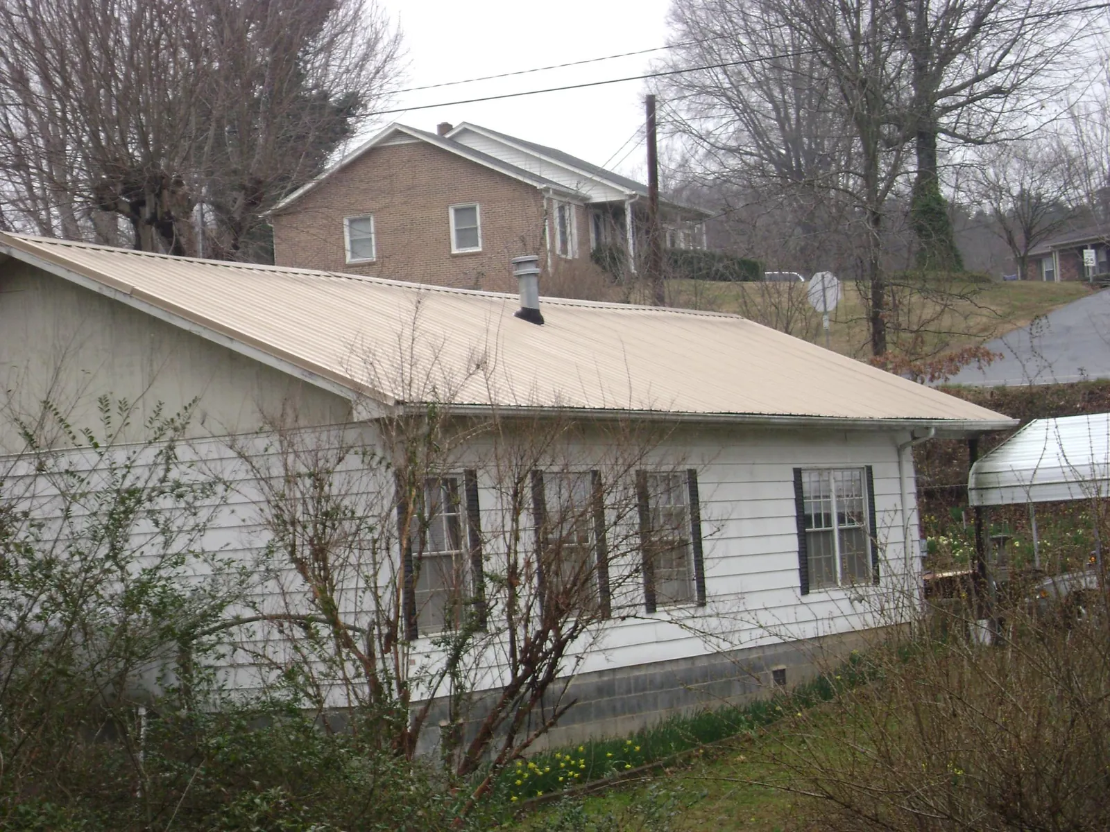 Tan metal roof on a white sided house set into a hillside — Commercial Roofing by Roofing Brothers in Melvin